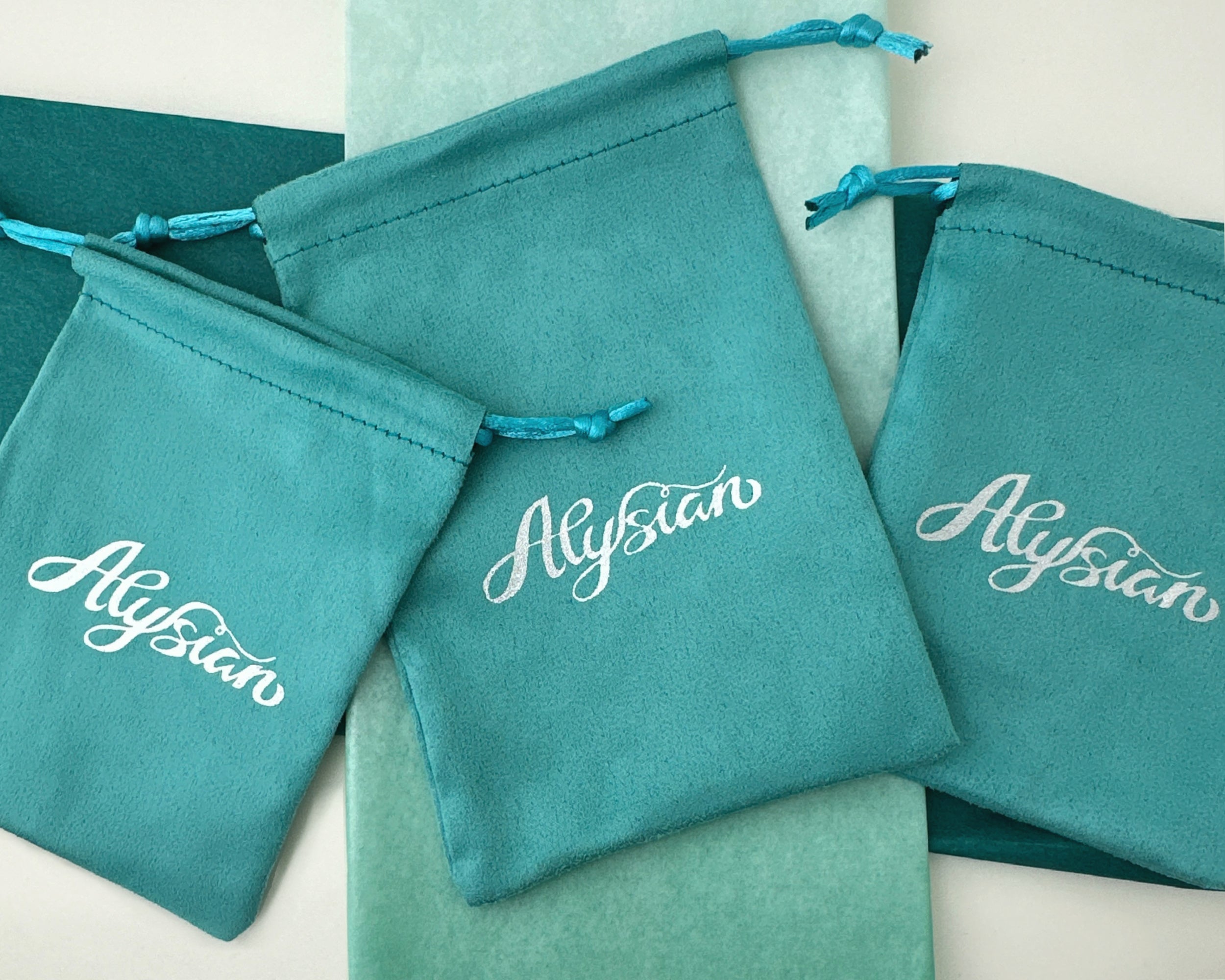 A few teal Alysian branded velvet jewelry pouches used for packaging.