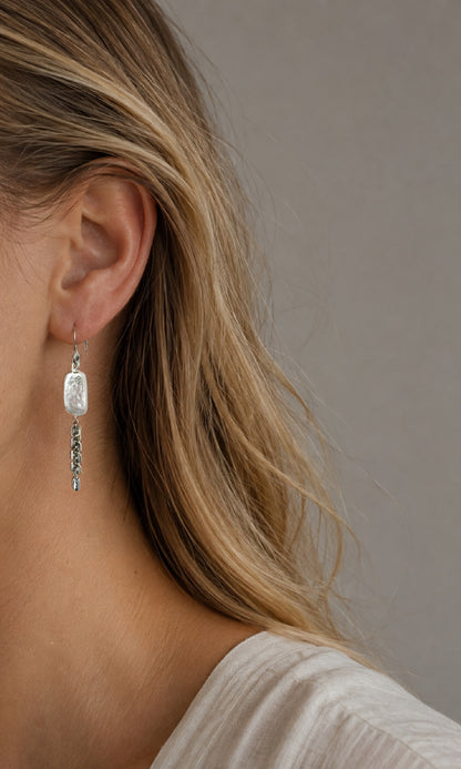 A close-up side profile of a woman wearing a linear dangle earring with a rectangular freshwater pearl and silver-tone chain. Hera Pearl Earring – A handcrafted earrings by Alysian.