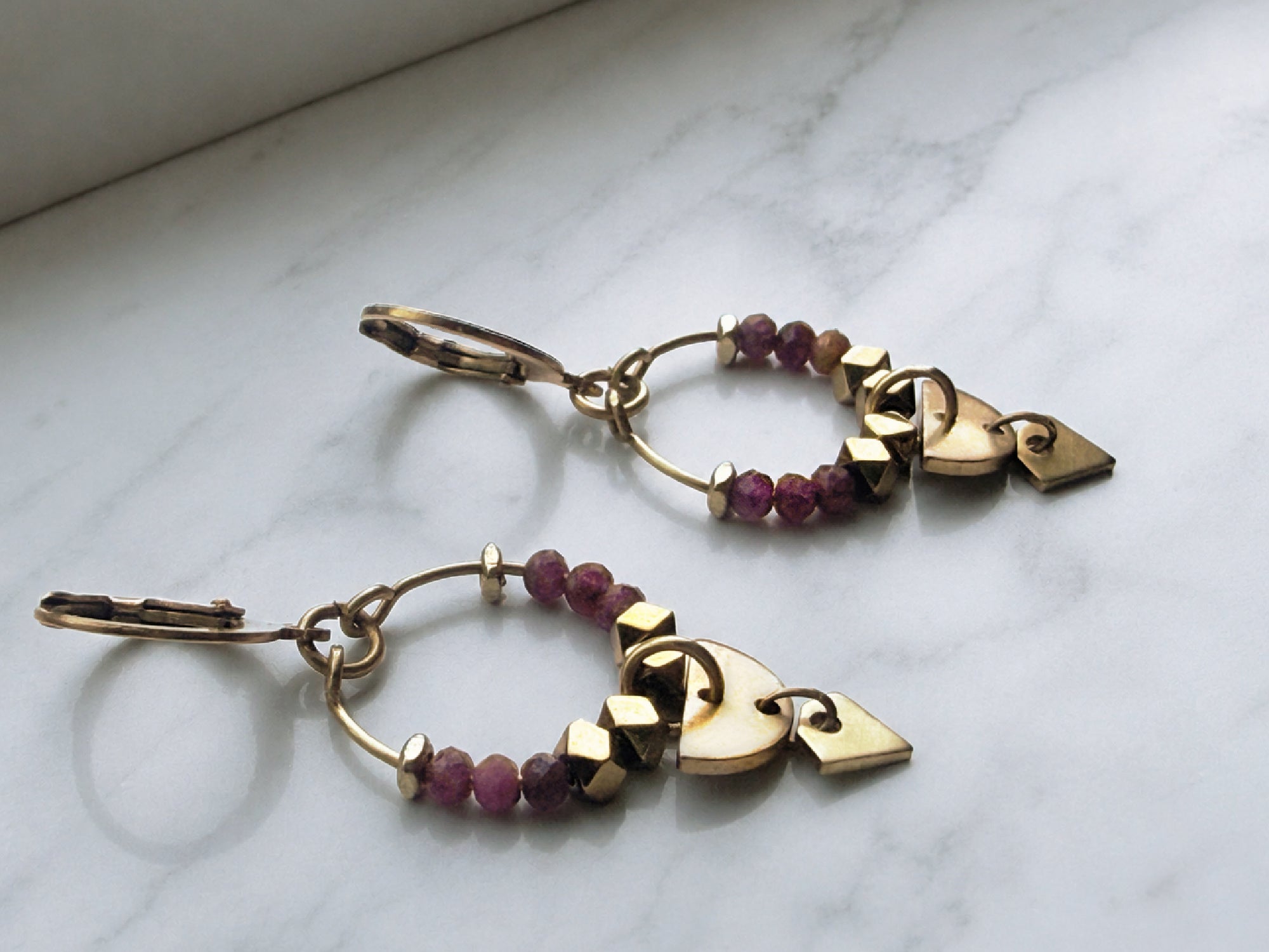 Petite ruby gemstone hoop earrings with gold-plated surgical steel leverback ear wires against a marble surface.