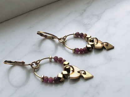 Petite ruby gemstone hoop earrings with gold-plated surgical steel leverback ear wires against a marble surface.
