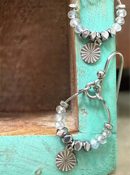 Close up of stainless steel Alysian labradorite beaded hoop earrings with metal accents on a turquoise surface.