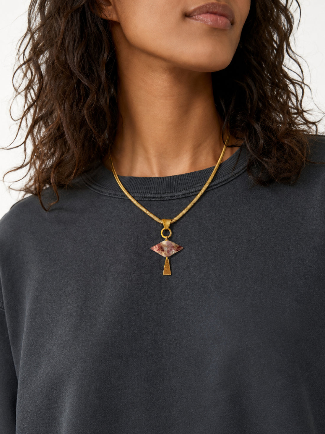 A close-up of a model wearing a brass flat snake chain necklace with a geometric gemstone pendant and vintage details, handcrafted by Alysian. 
