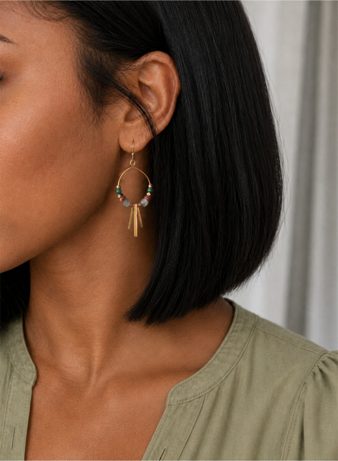 Close-up of a woman wearing the Alysian Soren Apatite gemstone beaded hoop earring with brass metal fringe.