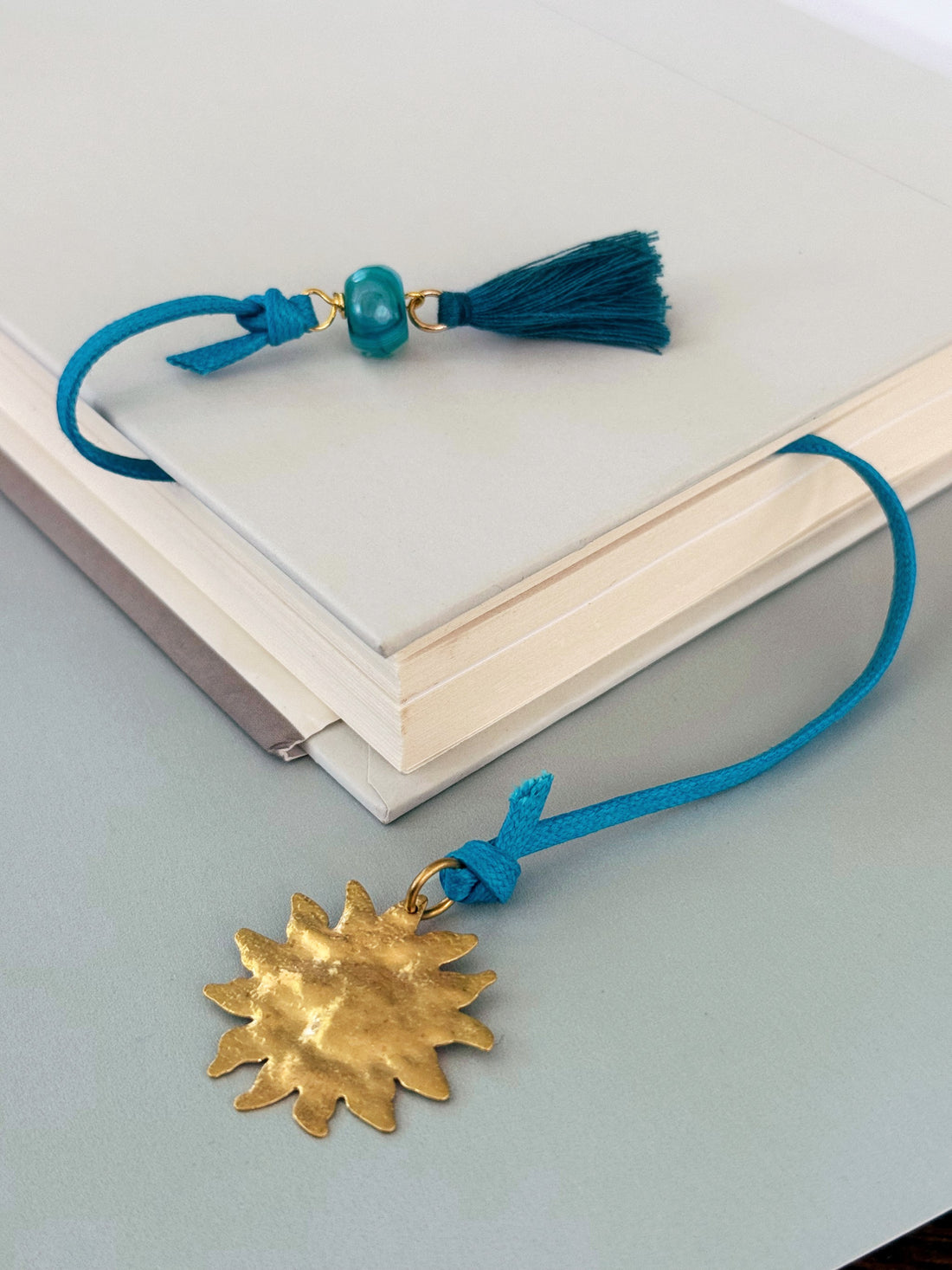 Blue tassel corded Solene  bookmark with agate and a gold sun charm extending from a book.