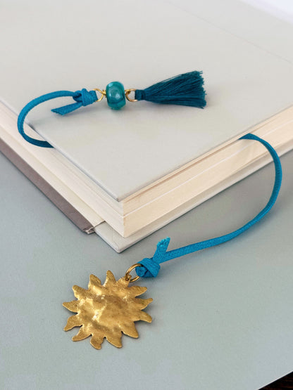 Blue tassel corded Solene  bookmark with agate and a gold sun charm extending from a book.